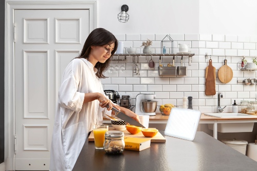 Woman making breakfast in a kitchen with a Lumie Vitamin L SAD light in front of her, receiving bright light therapy while she goes about her day.